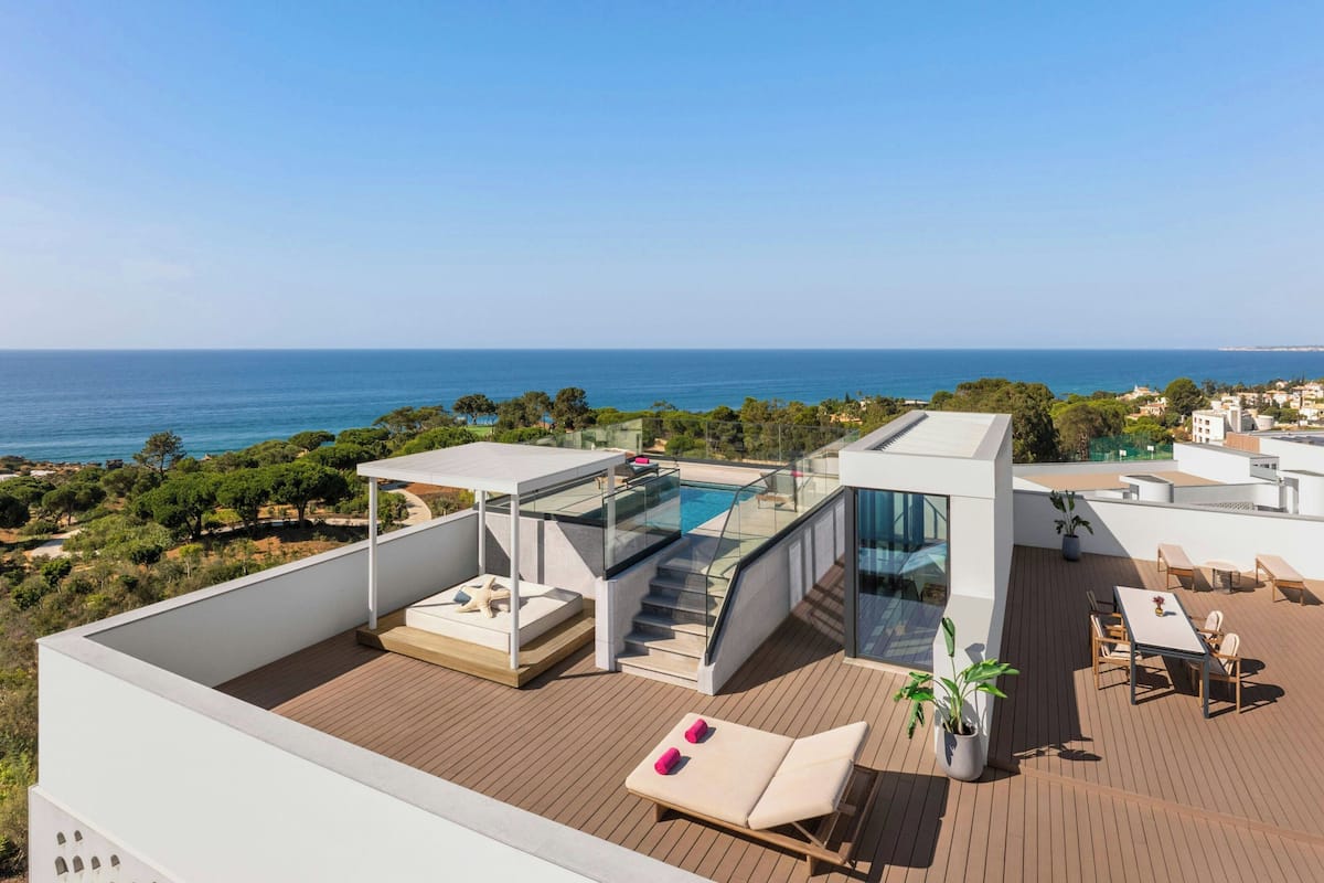 A rooftop terrace with a glass-enclosed infinity pool, outdoor seating, and a view of the sea.