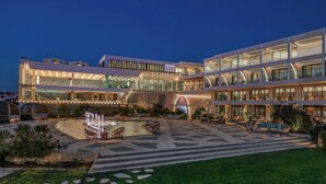 Un hotel moderno con un patio amplio, mobiliario exterior y una fachada bien iluminada.