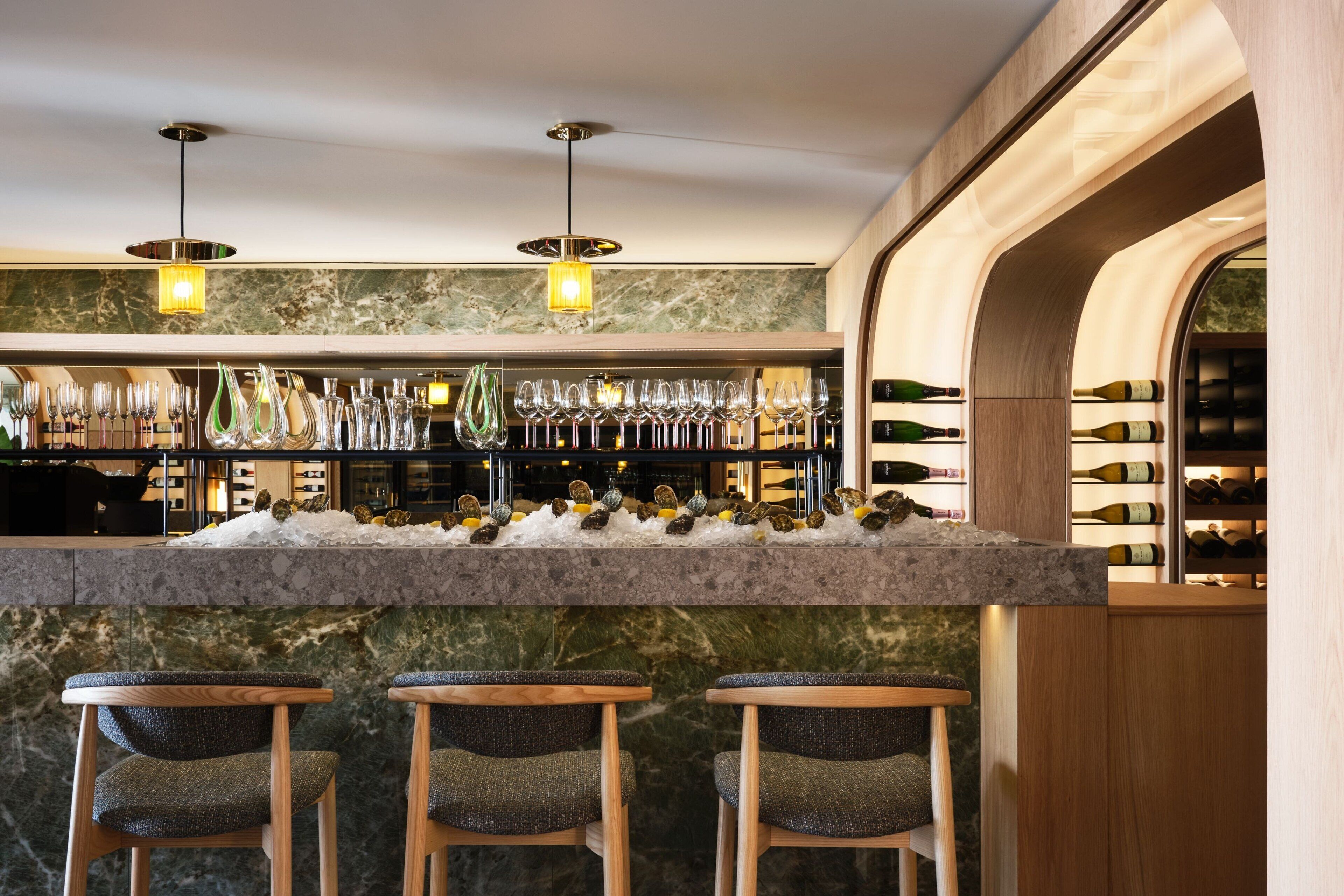 Angolo bar con un bancone in marmo, diverse bottiglie di vino e tre sgabelli da bar.