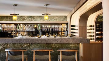 Angolo bar con un bancone in marmo, diverse bottiglie di vino e tre sgabelli da bar.
