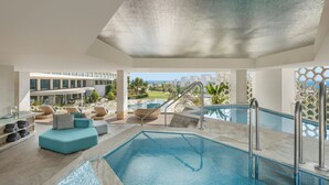 Un área de piscina interior moderna con vistas despejadas al océano, una zona de estar con asientos y un bar junto a la piscina.