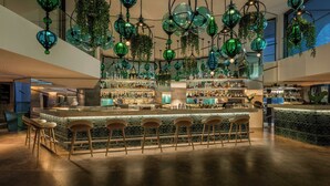 Un bar moderno con una isla central, múltiples lámparas de cristal verde colgantes y una variedad de taburetes de bar.