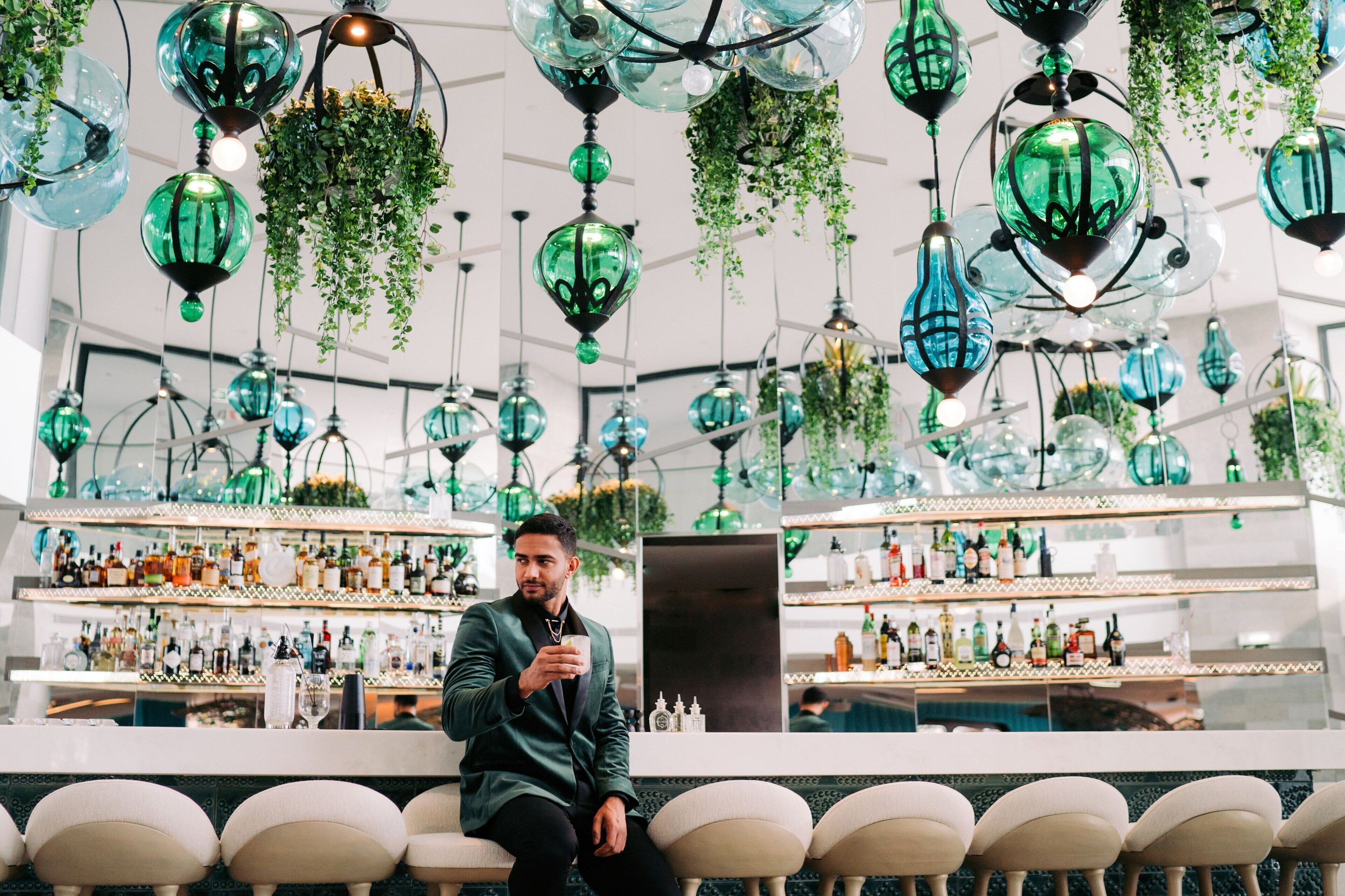 Un espace bar agrémenté de lampes suspendues en verre vert et d’étagères remplies de bouteilles.