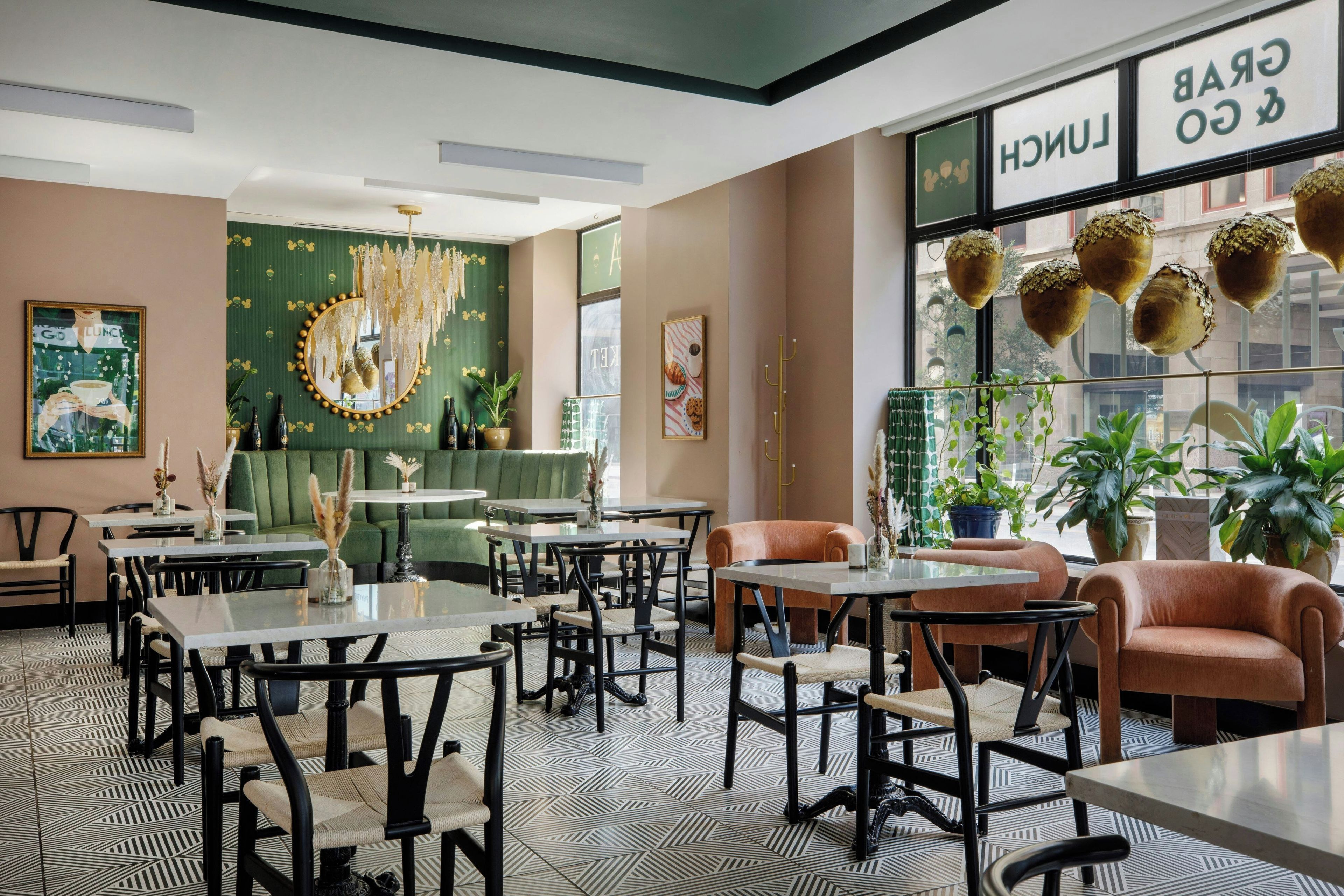 Un intérieur moderne doté de plusieurs espaces de détente, comprenant des tables et des chaises, ainsi qu’une grande fenêtre ornée de plantes suspendues décoratives.
