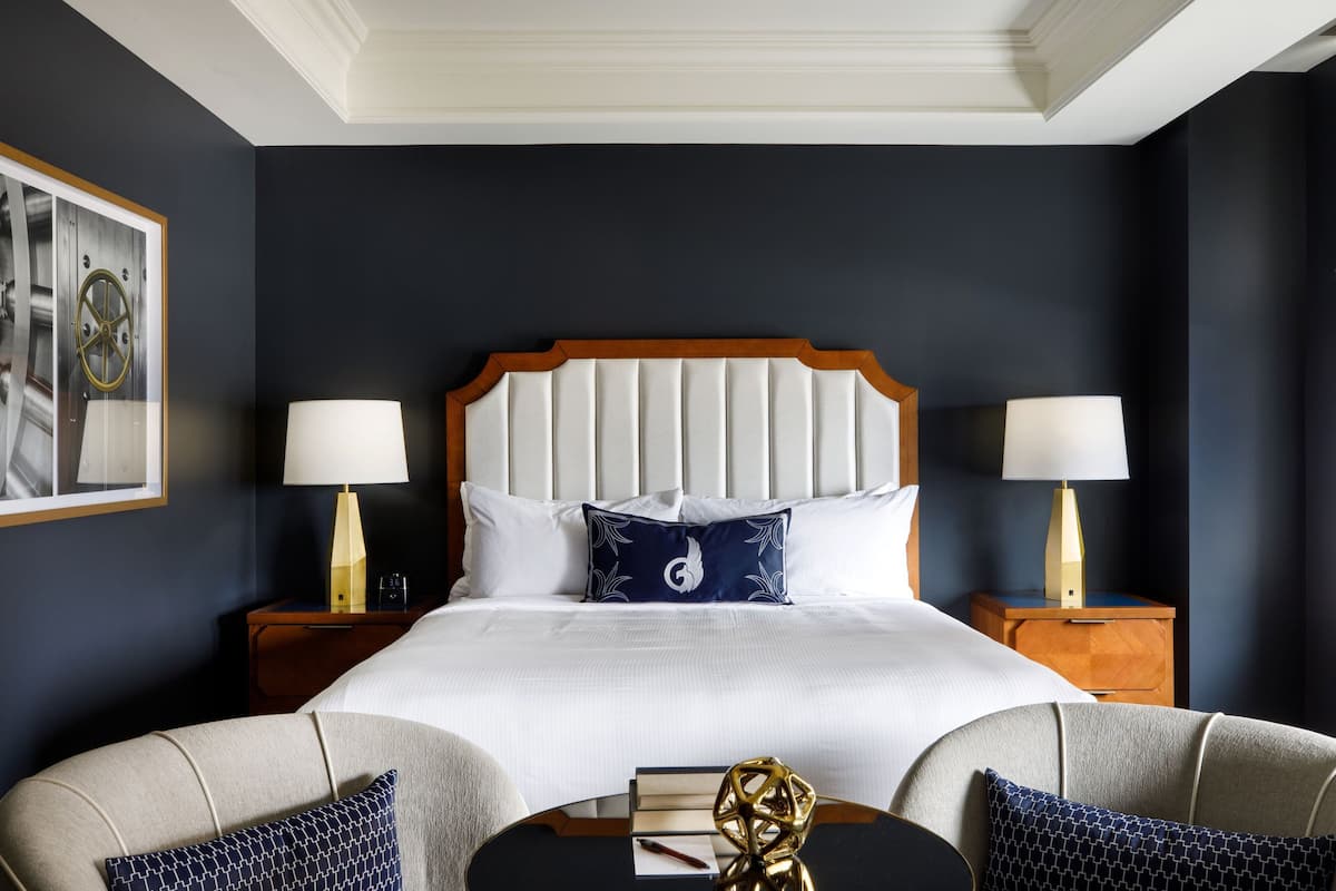 A hotel room with a large bed, two bedside tables with lamps, a small table with a decorative item, and a framed picture on the wall.