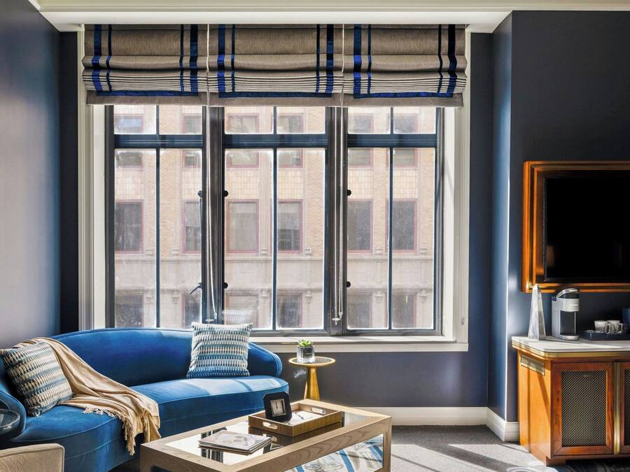 A living room with a blue sofa, a coffee table, and a large window with blinds.