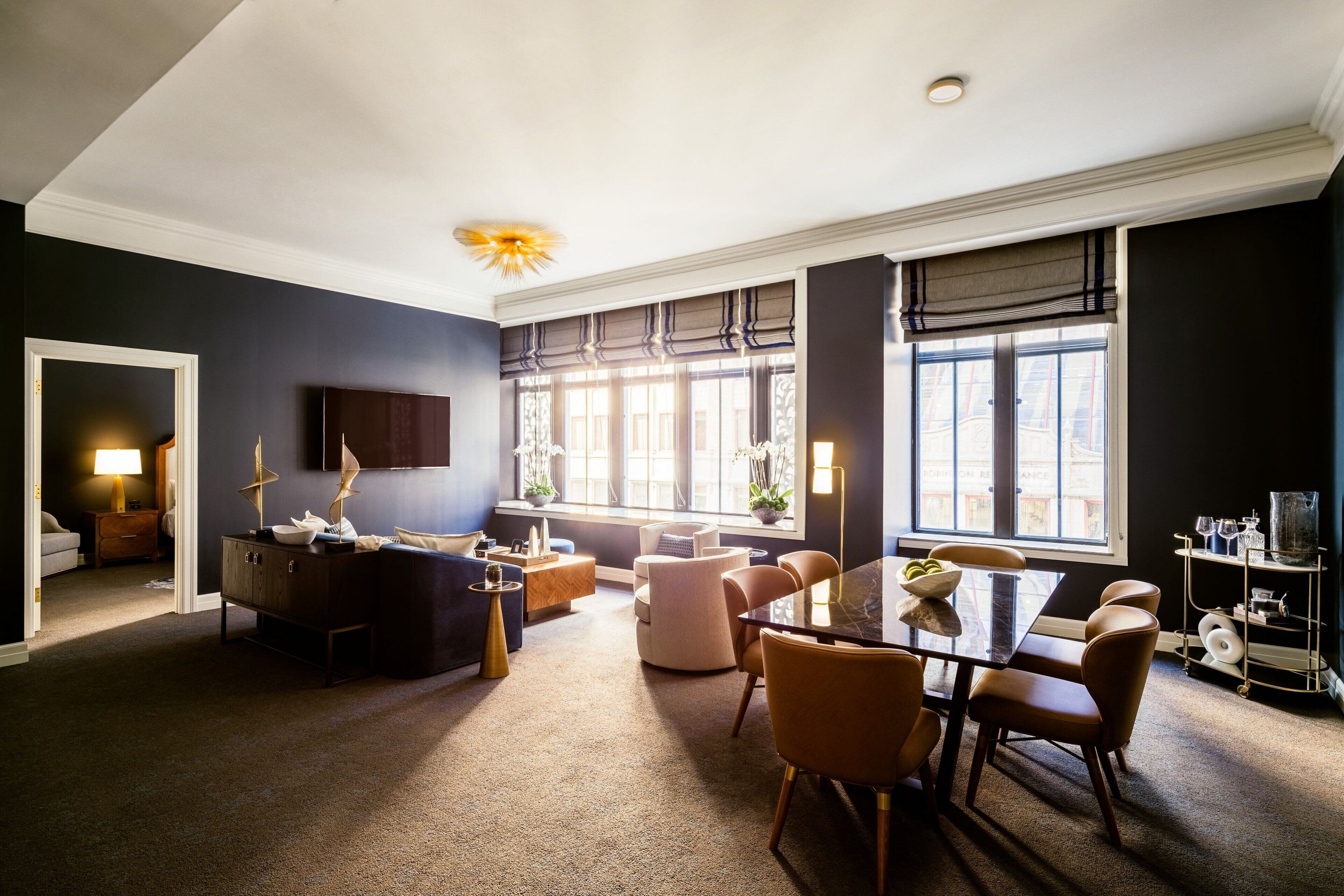 A modern living room with a dark wall, a dining area with a glass table, and a cozy seating area with a sofa and armchairs.