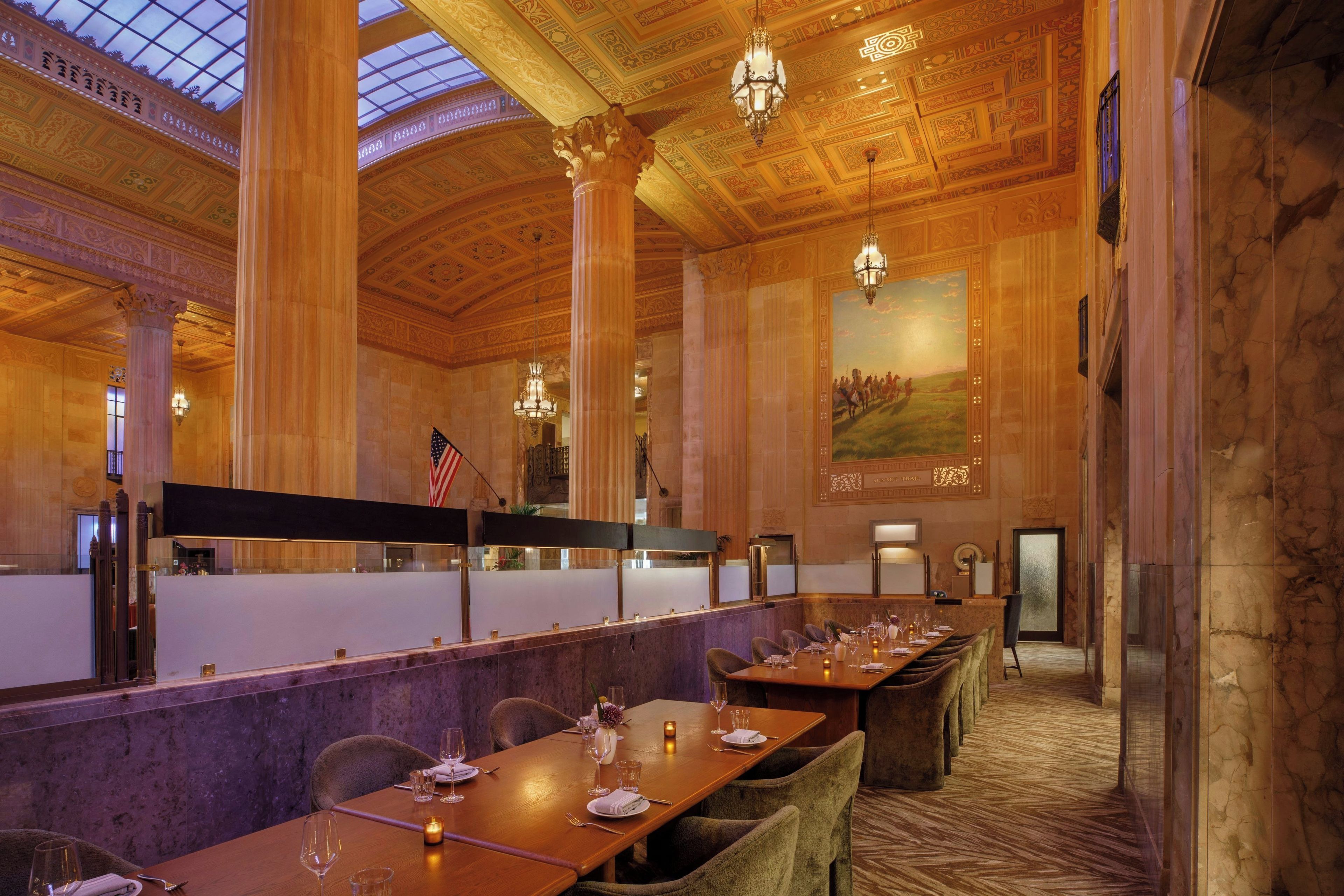 A formal dining area with long tables, chairs, and chandeliers.