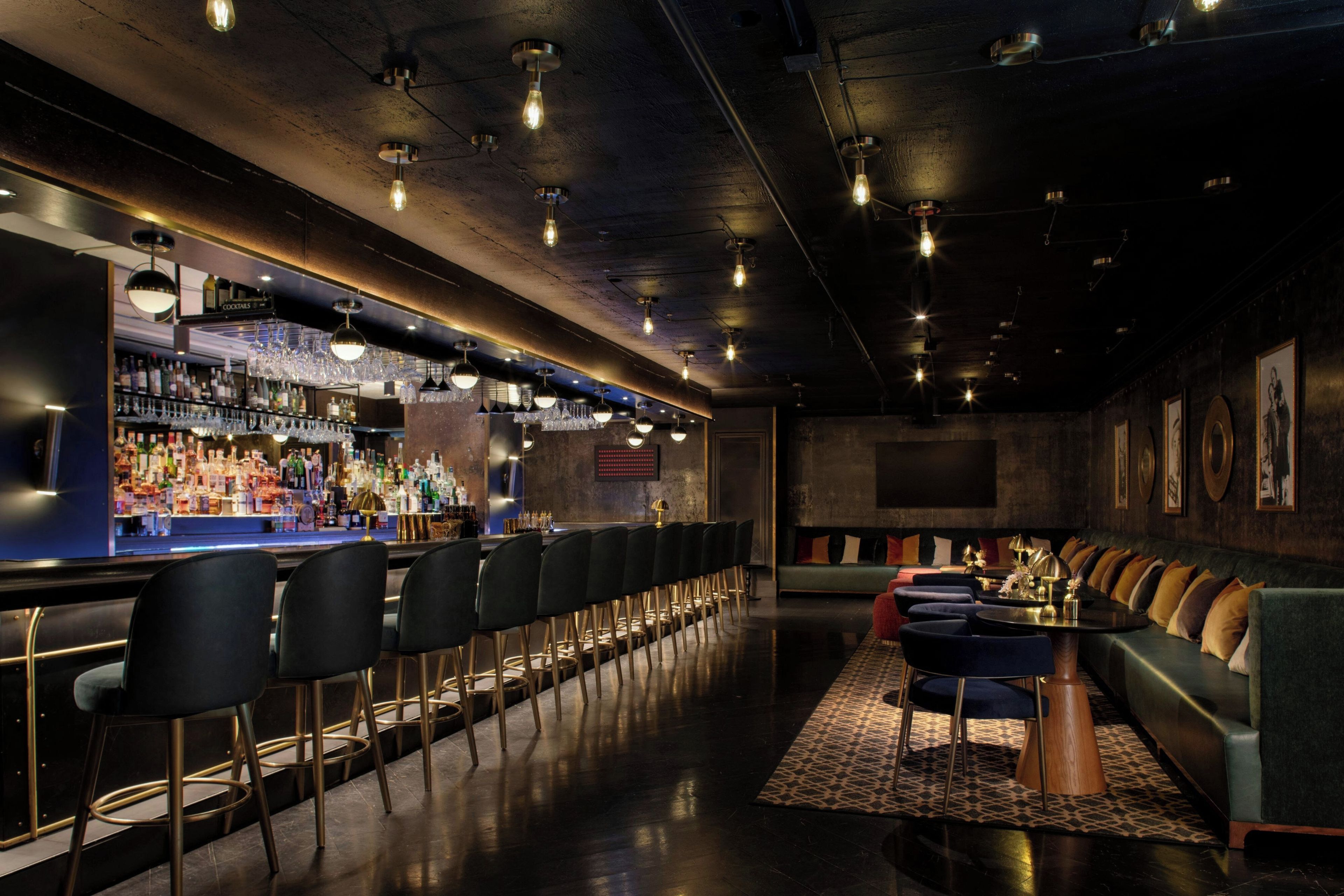 A bar area with a long counter, multiple bar stools, and a seating area with couches and a patterned rug.