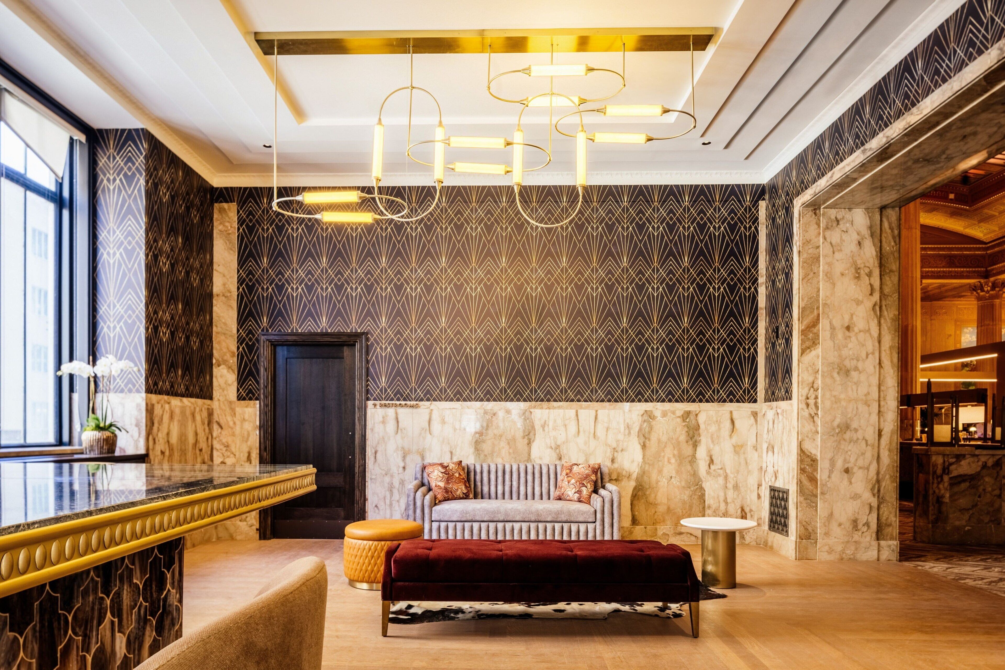 A lobby with a marble reception desk, a plush sofa with patterned cushions, and a modern chandelier.