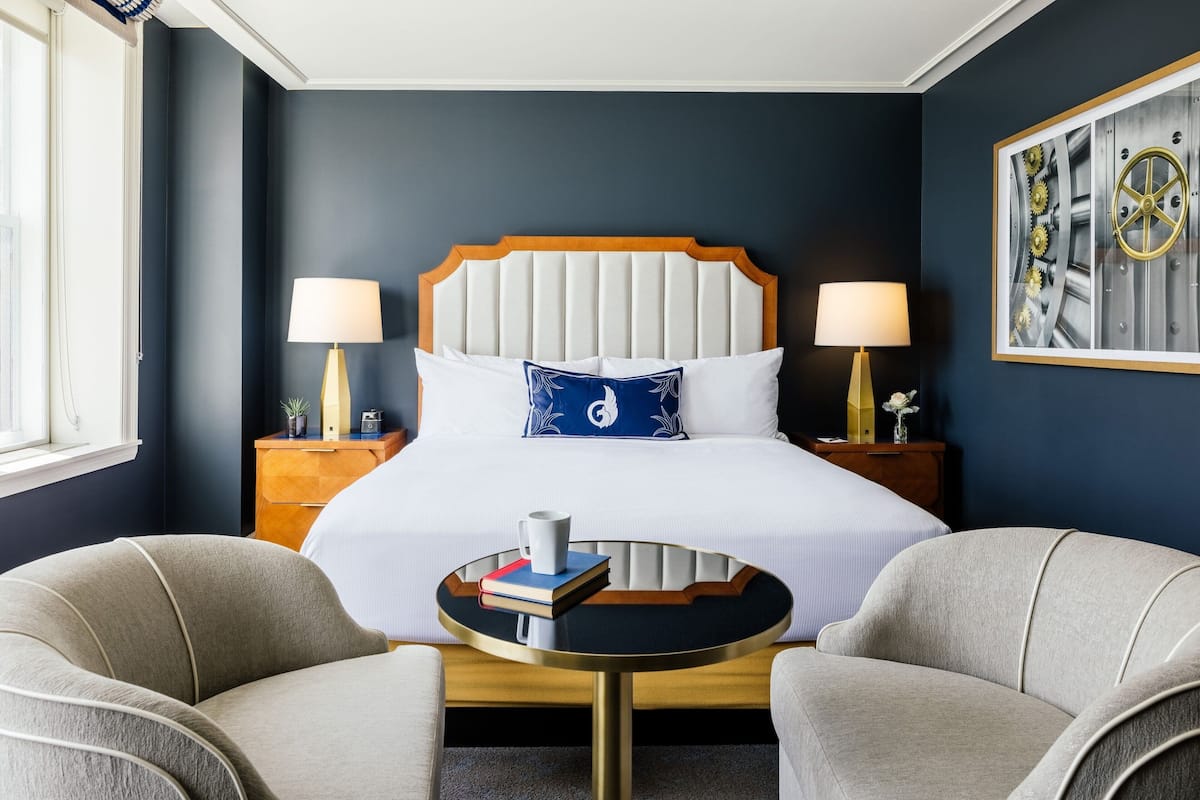 A hotel room with a large bed, two bedside lamps, a round table, and two armchairs.