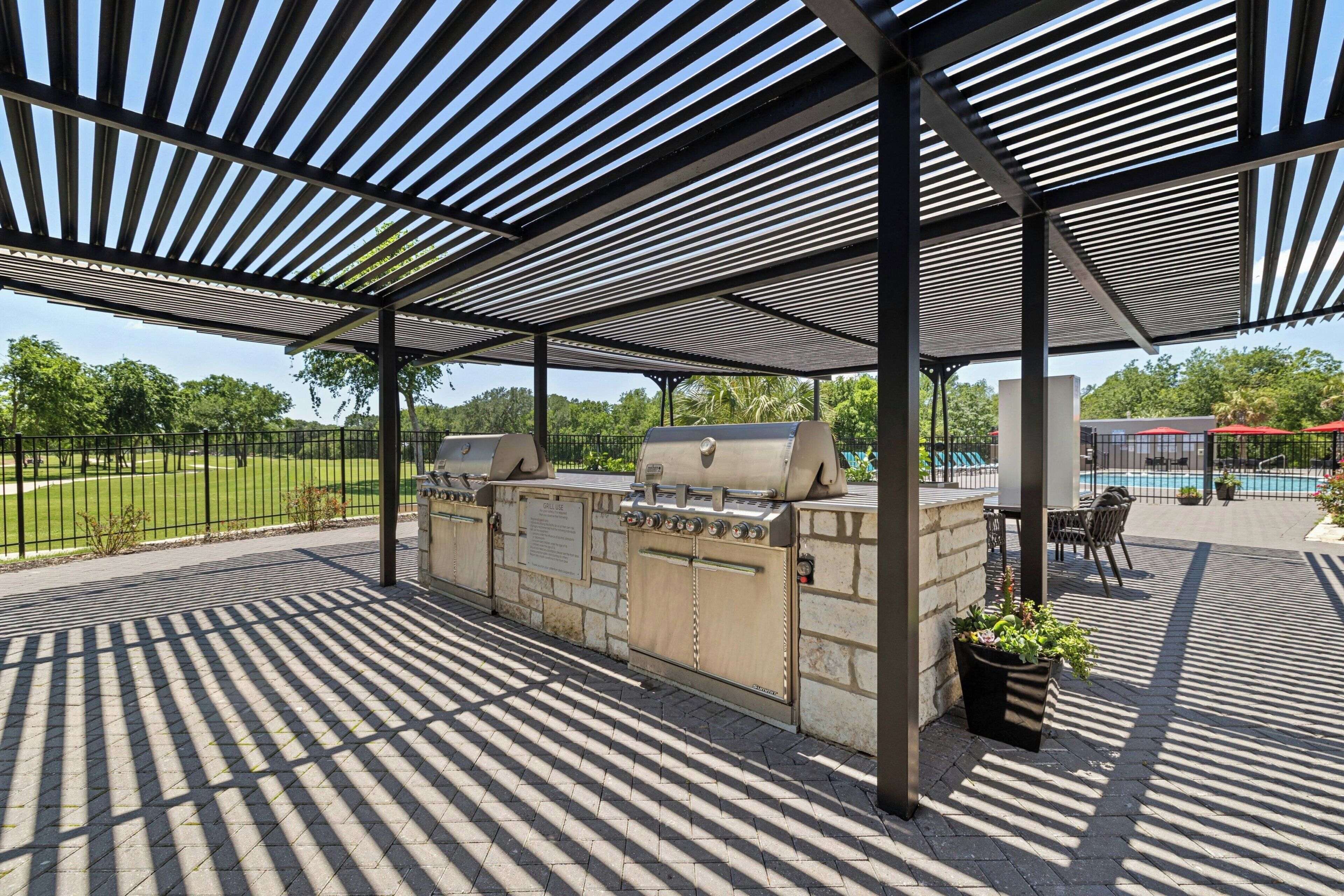 An outdoor grill station with a metal roof and a paved patio area.