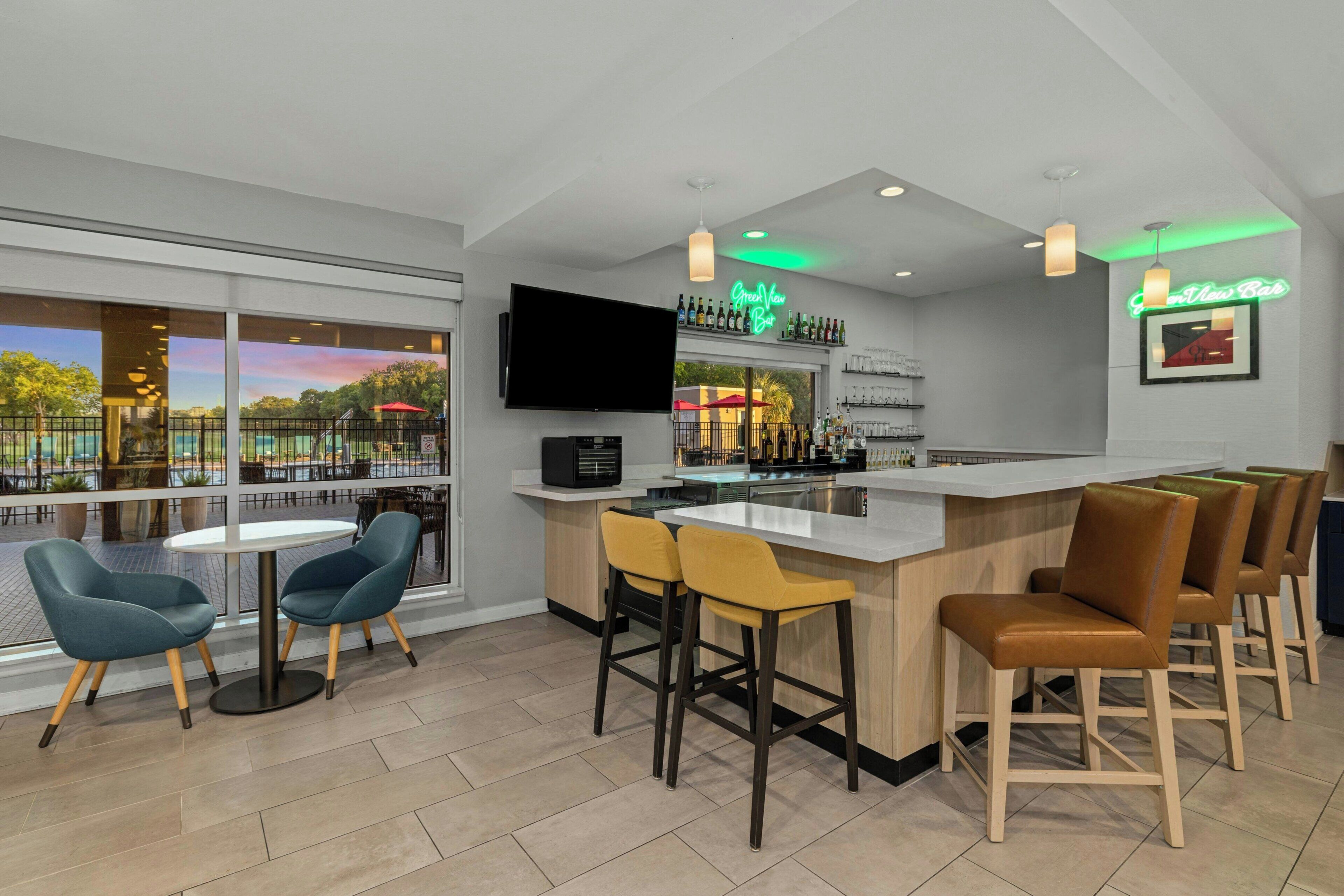A bar area with a flat-screen TV, a neon sign, and a view of the outdoors.