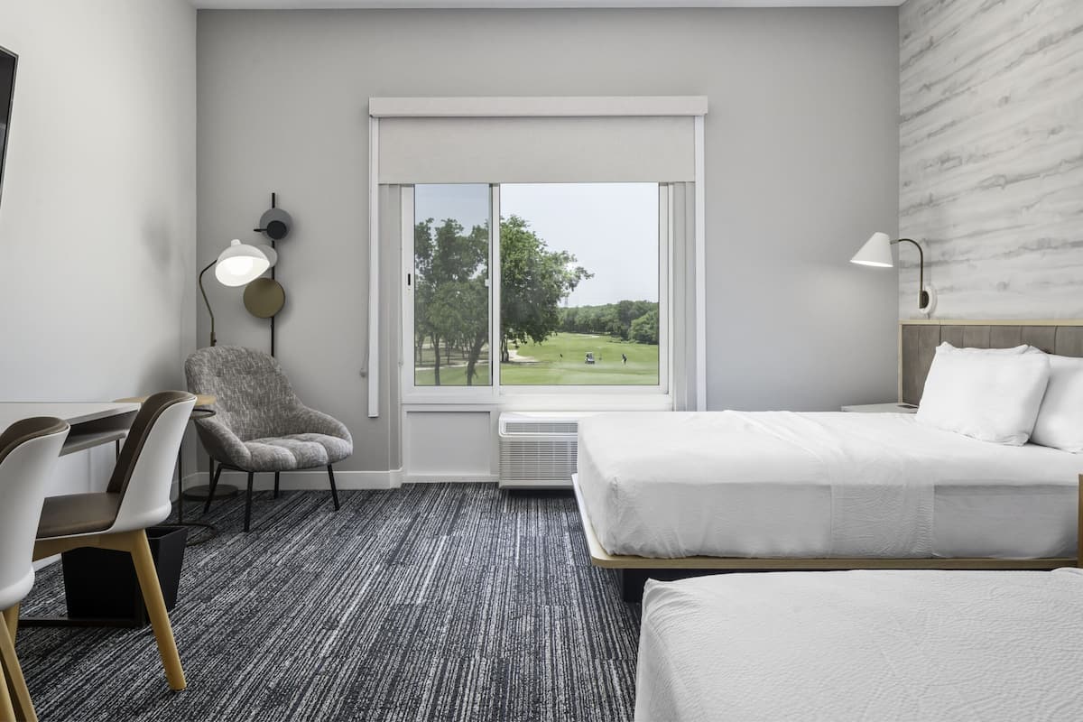 Une chambre d’hôtel équipée d’un lit, d’un bureau, d’une chaise, d’une lampe et d’une fenêtre donnant sur un parc.