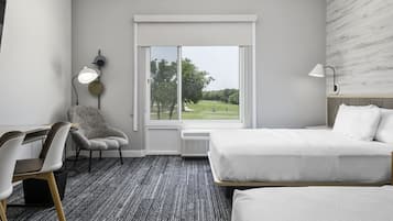 A hotel room with a bed, a chair, a desk, a lamp, and a window with a view of a golf course.