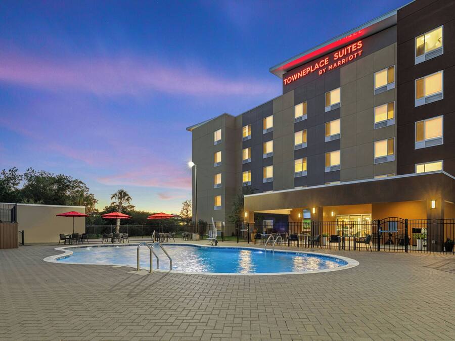 A hotel with a swimming pool, outdoor seating, and a clear sky.