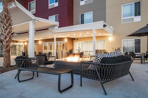 An outdoor seating area with wicker furniture, a fire pit, and a covered walkway.