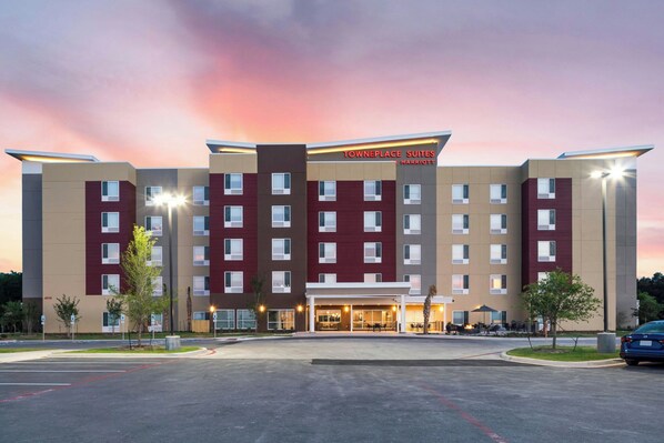 A multi-story hotel with a prominent entrance, a parking lot, and a clear sky.