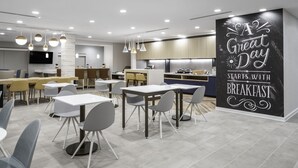 A modern dining area with tables and chairs, a kitchen in the background, and a motivational wall with text. - TownePlace Suites by Marriott San Antonio Universal City/Live Oak (Selma)