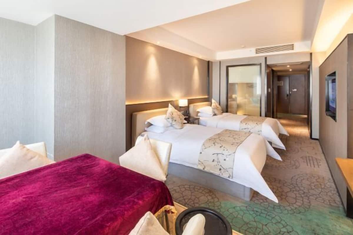Ein Hotelzimmer mit zwei Betten, einem roten Sessel, einem kleinen Tisch und einem Spiegel.