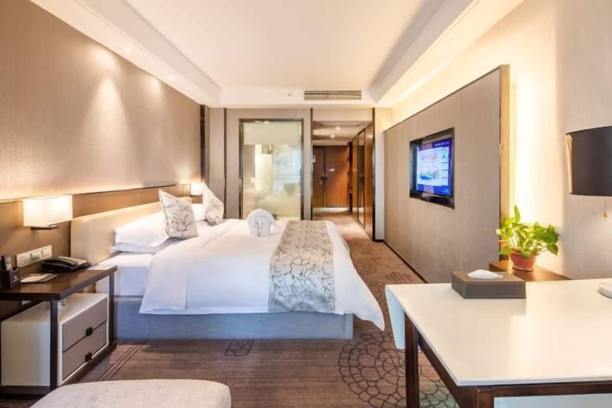 Ein Hotelzimmer mit Bett, Nachttisch, Lampe, Fernseher und einem kleinen Tisch mit Pflanze.