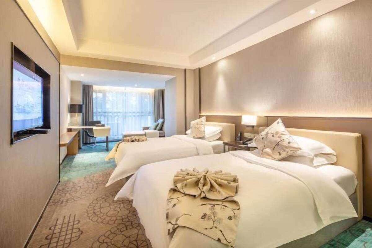 Une chambre d’hôtel avec deux lits, un bureau, une chaise et un téléviseur fixé au mur.