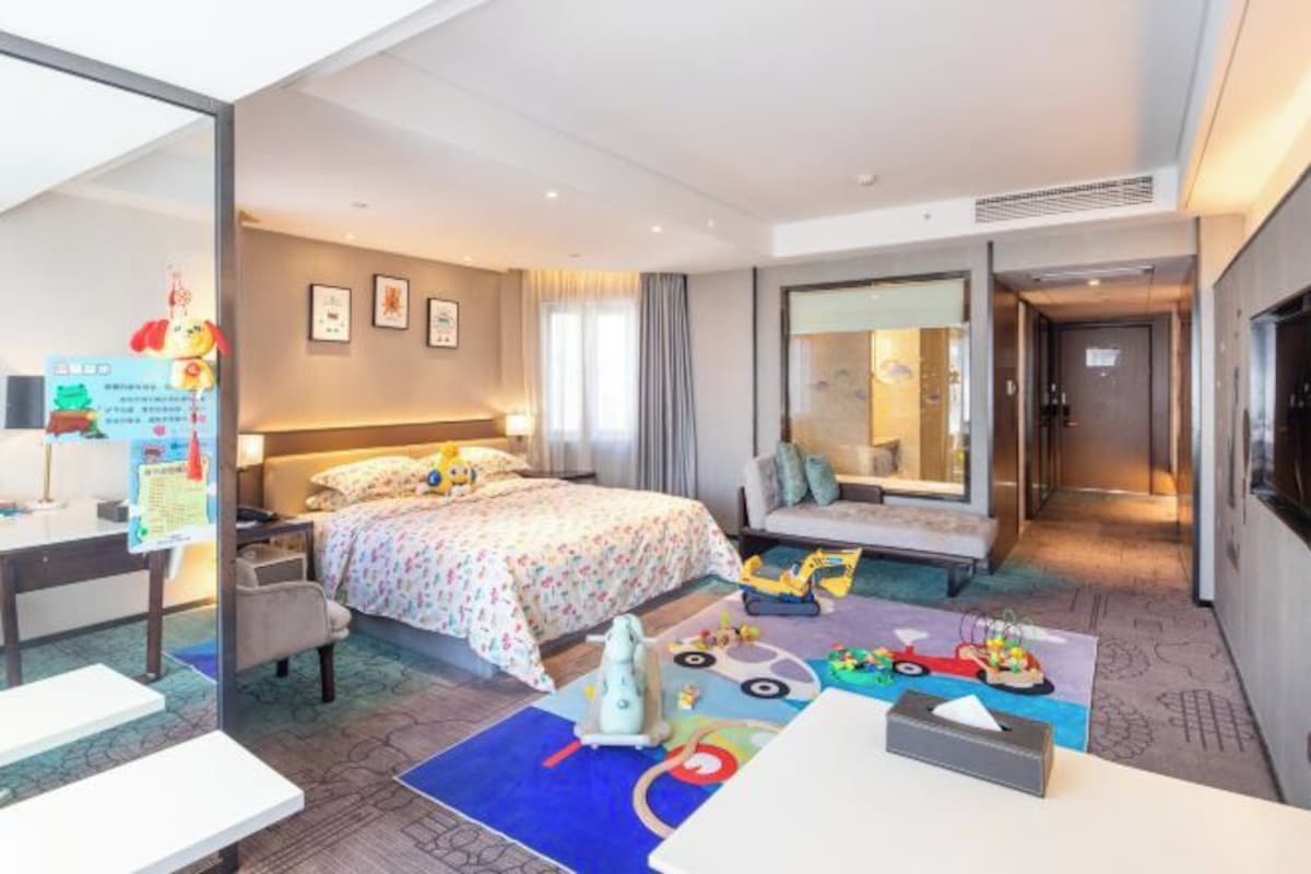 Quarto de hotel com cama, mesa de cabeceira, cadeira e escrivaninha com um computador.