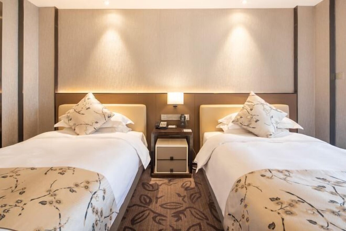 A hotel room with two beds, each with a pillow and a bedside table.