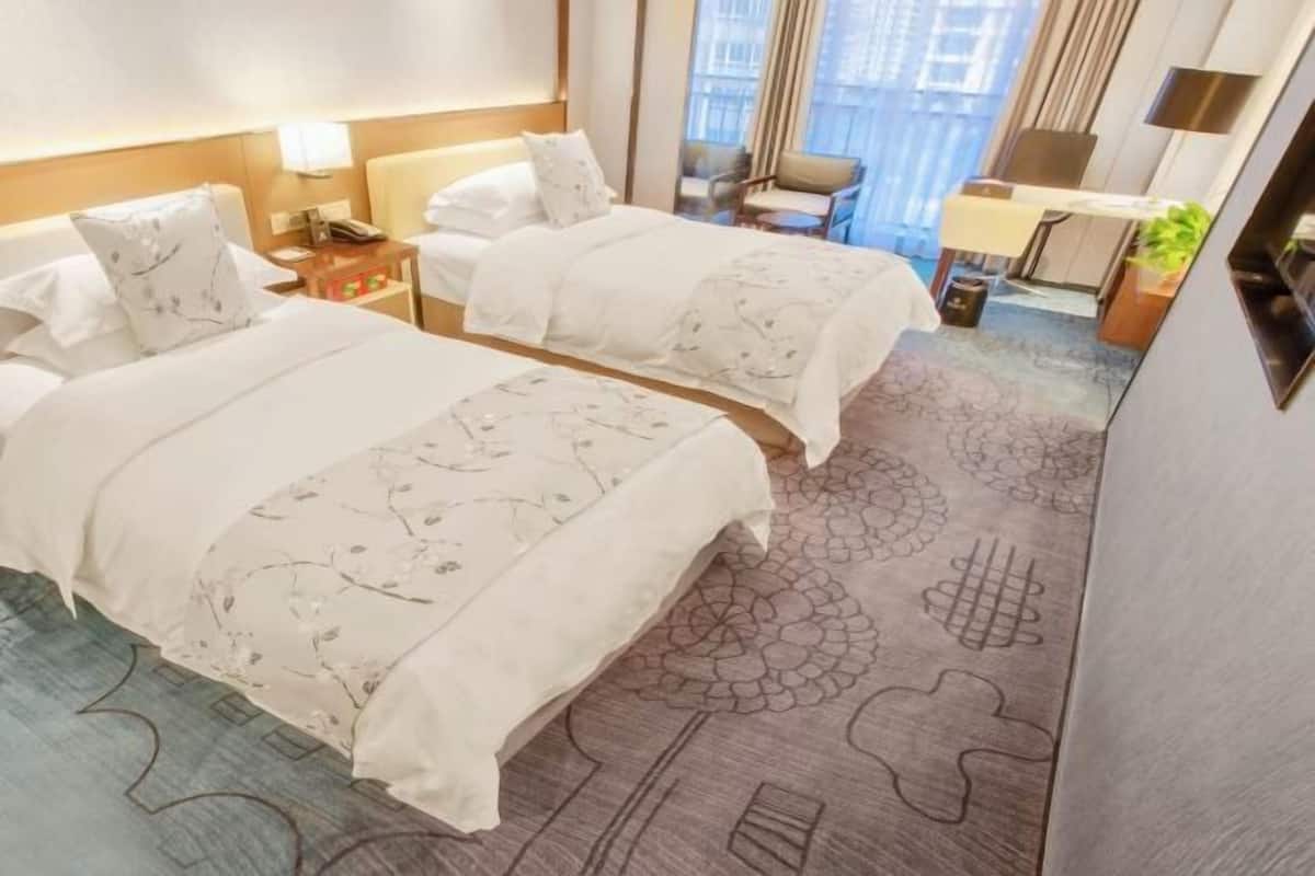Ein Hotelzimmer mit zwei Betten, einem Schreibtisch, einem Stuhl und Blick auf die Stadt.