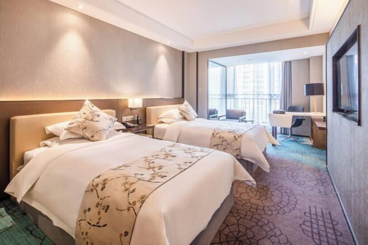 Ein Hotelzimmer mit zwei Betten, einem Schreibtisch, einem Stuhl und einem Fernseher.
