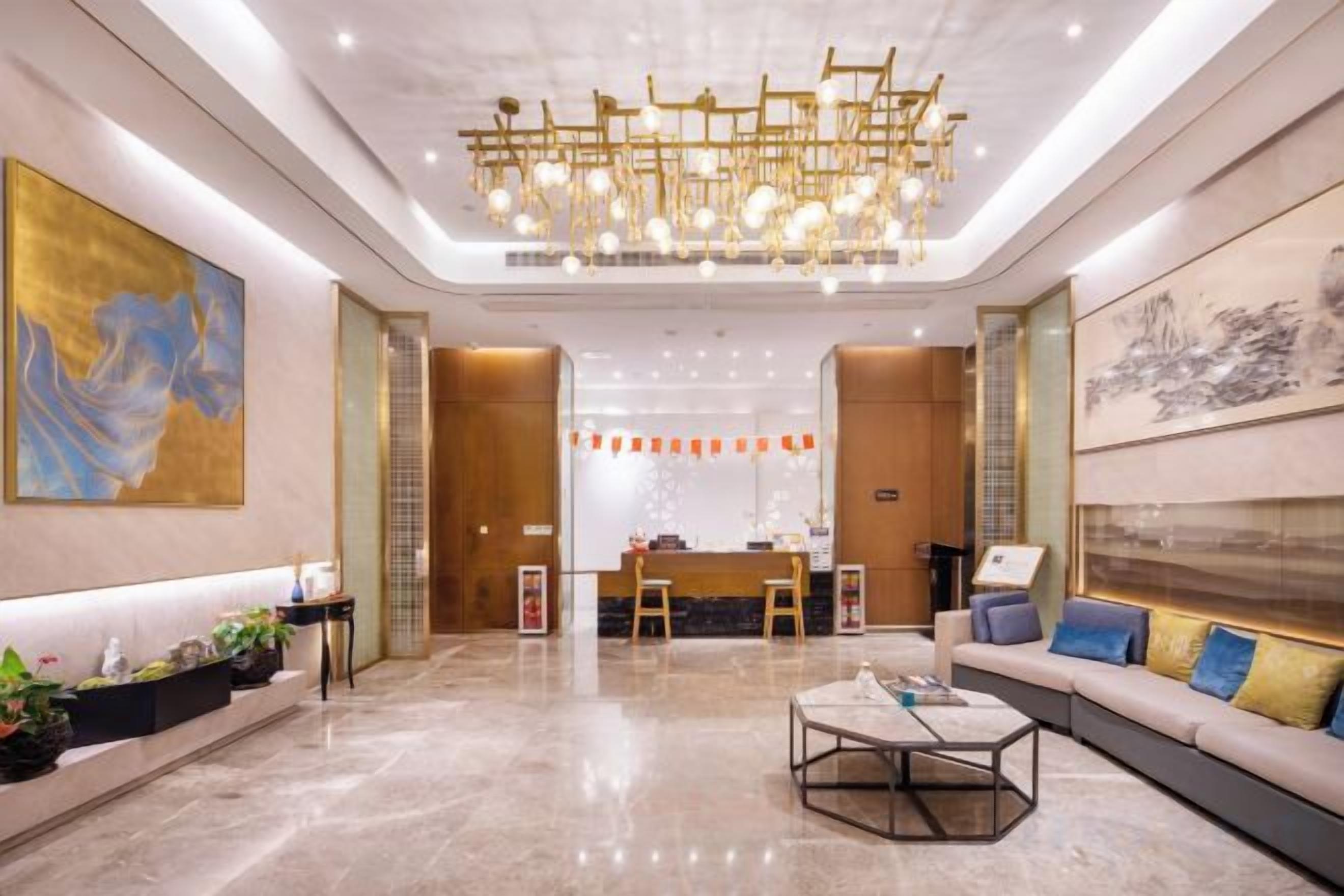 A hotel lobby with a reception desk, seating area, and a modern chandelier.