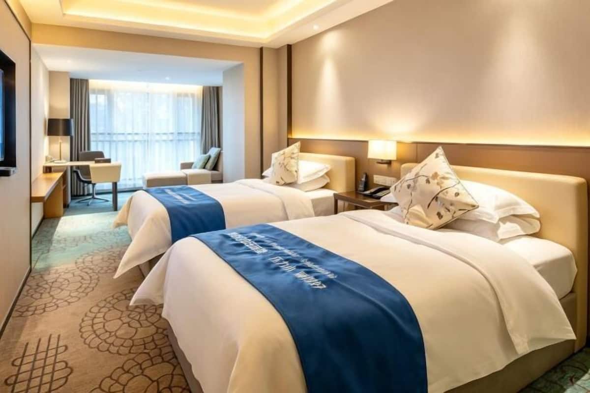 Ein Hotelzimmer mit zwei Betten, einem Schreibtisch, einem Stuhl und Blick ins Freie.