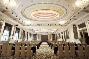 Un salón de conferencias con filas de sillas, una lámpara de candelabro y una alfombra estampada.