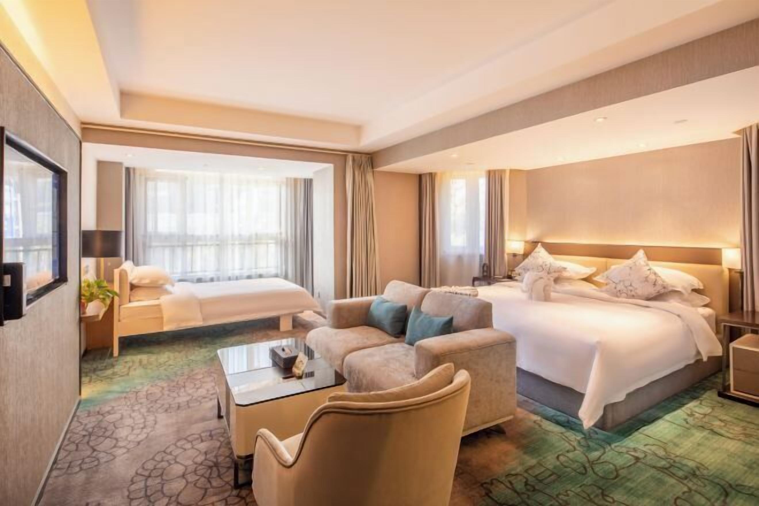 A hotel room with a bed, a sofa, a chair, a small table, and a TV.