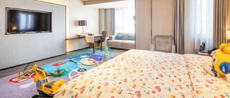 A hotel room with a large bed, a TV mounted on the wall, a desk with a chair, and a window with curtains.