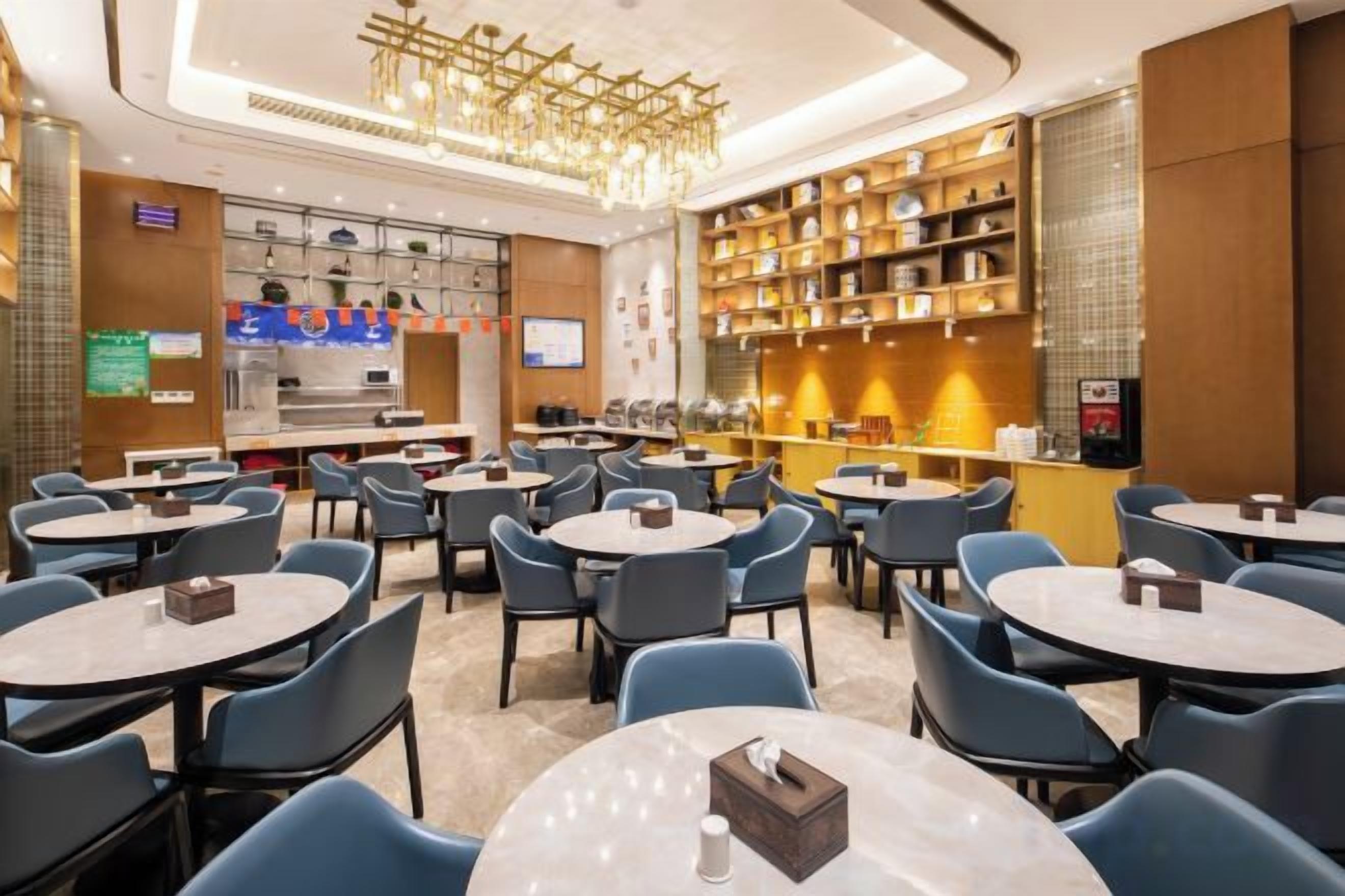 Un restaurante de hotel con mesas redondas, sillas, una zona de bar y una pantalla de televisión.