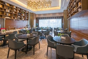 A hotel lobby with round tables, chairs, bookshelves, and a chandelier. - New Glory Holiday Inn (Jurong)