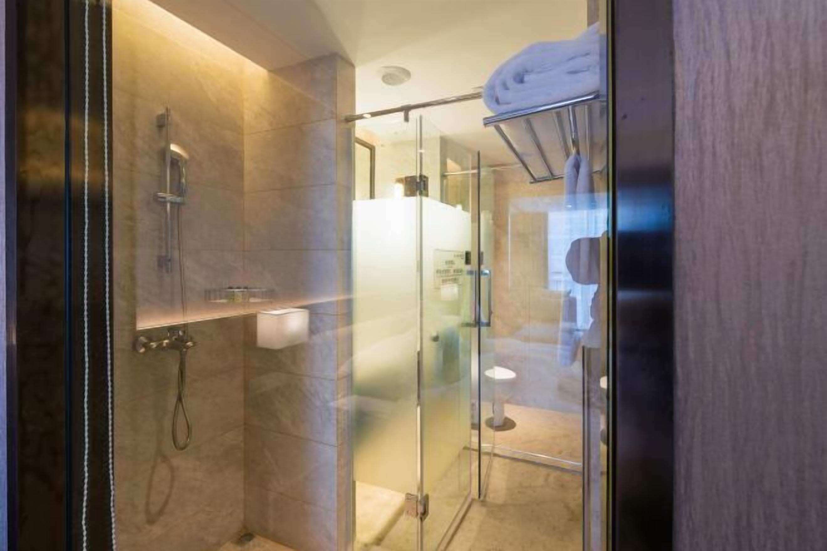 A glass-enclosed shower area with a towel rack and a toilet visible through the glass.
