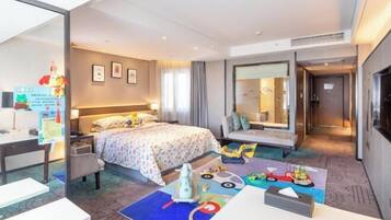 Ein Hotelzimmer mit Bett, Nachttisch, Sessel, Schreibtisch und einer bunten Spielecke.