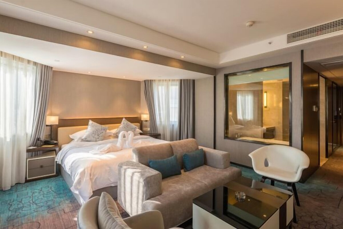 A modern hotel room with a large bed, a sofa, a coffee table, and a mirror.