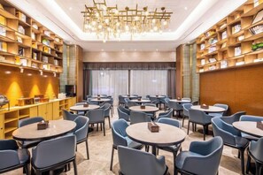 A hotel dining area with round tables and chairs, a chandelier, and bookshelves along the walls.