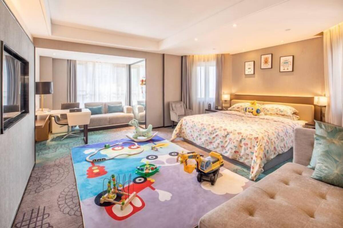 Ein Hotelzimmer mit einem großen Bett, einem Schreibtisch, einem Stuhl und einem bunten Spielbereich.