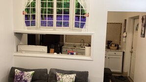 Ein Zimmer mit einer Couch, einem Fenster mit Blick auf Bäume, einer Küchenzeile und einer Tür.