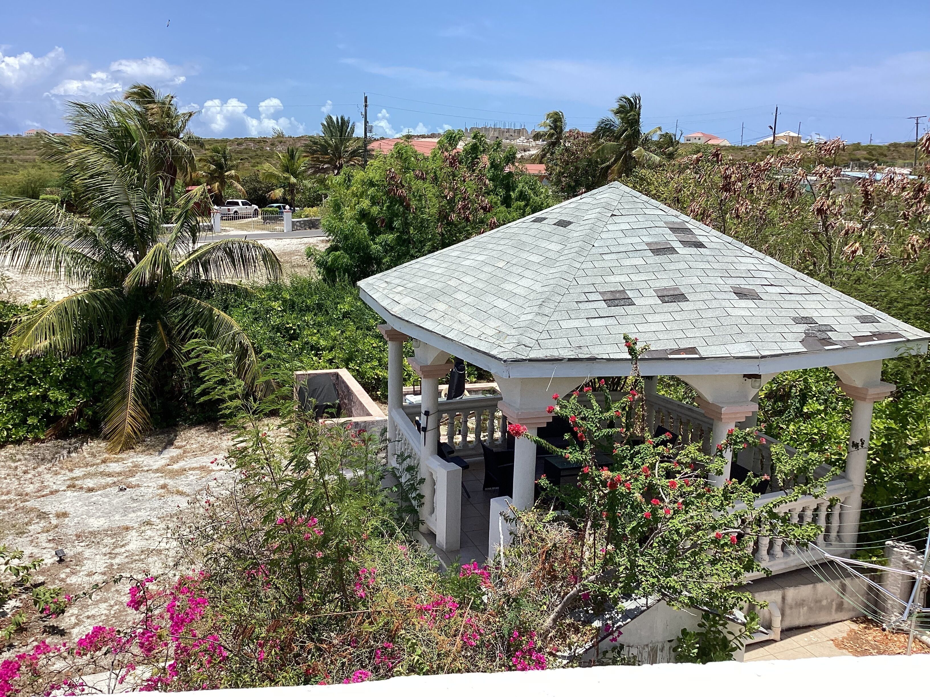 A gazebo with a tiled roof, surrounded by lush greenery and flowering plants.