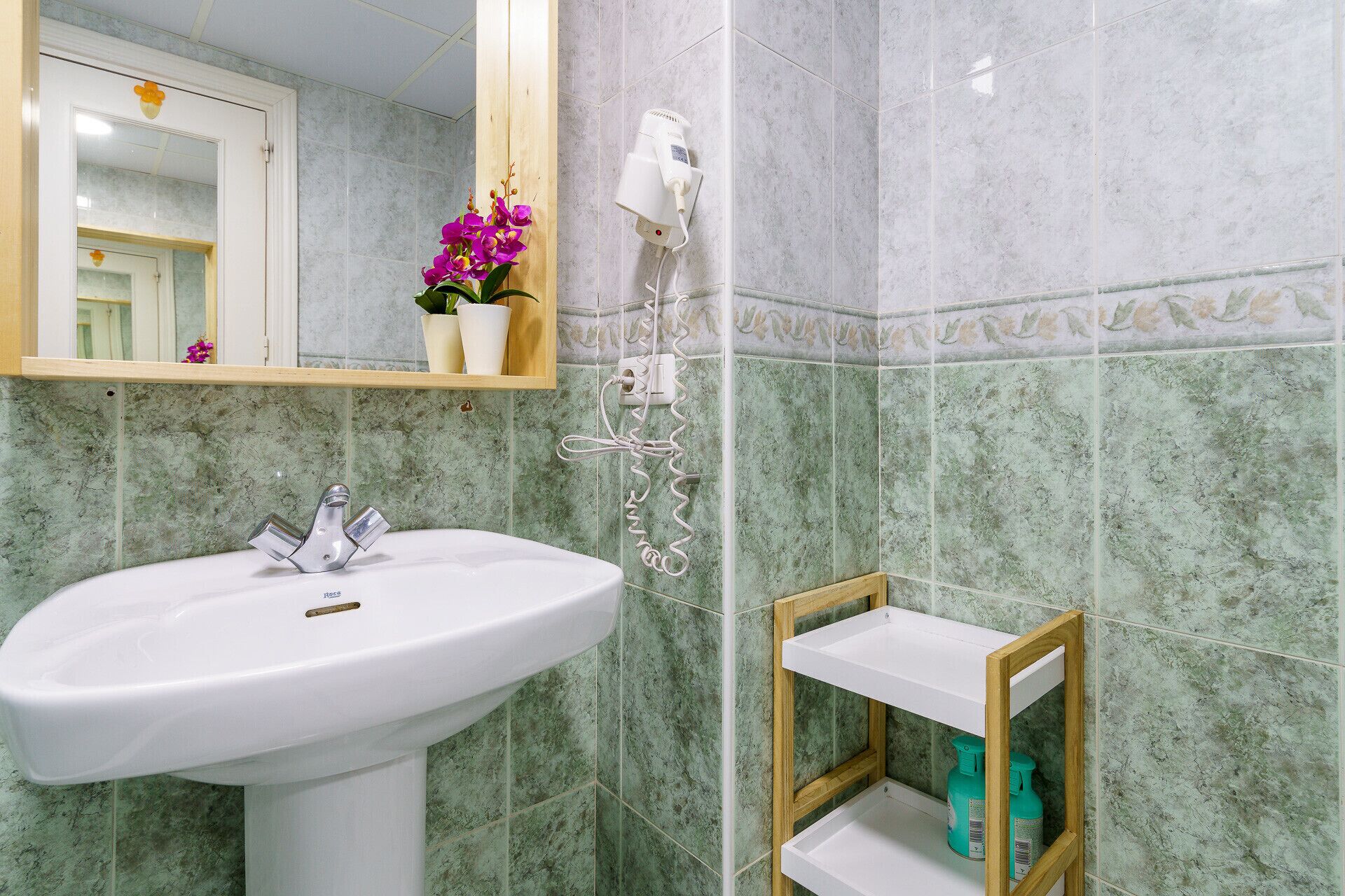 Een badkamer met een wit wastafel, een spiegel en een föhn aan de muur.