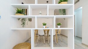 Ein modernes Interieur mit einer weißen Regalanlage, die verschiedene Pflanzen präsentiert, sowie einem Essbereich mit Holztischen und -stühlen.