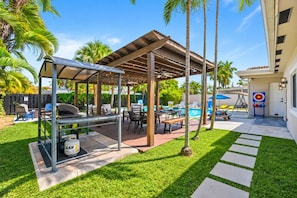 A covered outdoor patio with a grill, seating area, and a pool. - Deluxe 5BR/3BA Villa in Hollywood Lakes near Beach (Hollywood)