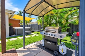 Een achtertuin met een draagbare barbecue, een overdekte zithoek en een terras.