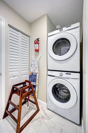 A laundry room with a stacked washer and dryer, a wooden ladder, and a fire extinguisher on the wall. - Deluxe 5BR/3BA Villa in Hollywood Lakes near Beach (Hollywood)