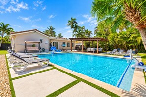 A swimming pool with lounge chairs, a covered seating area, and palm trees in the background. - Deluxe 5BR/3BA Villa in Hollywood Lakes near Beach (Hollywood)